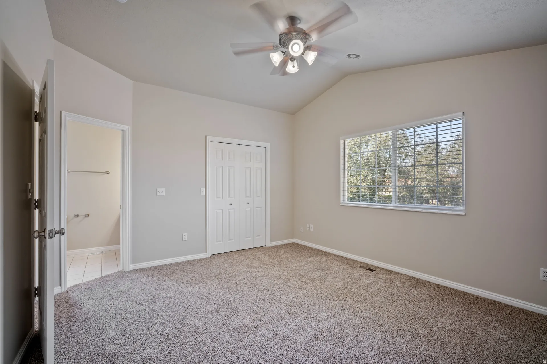 Vaulted ceiling with a ceiling fan, carpet flooring, a window with horizontal blinds, and a bi-fold closet door