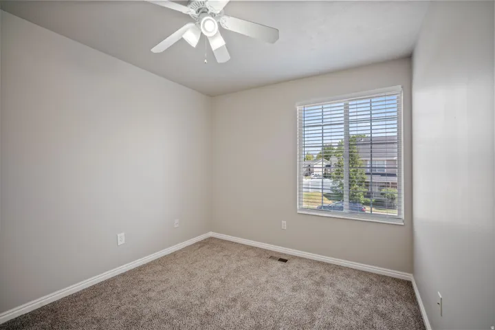 Neutral wall paint, textured carpet, window with blinds, ceiling fan with integrated lighting