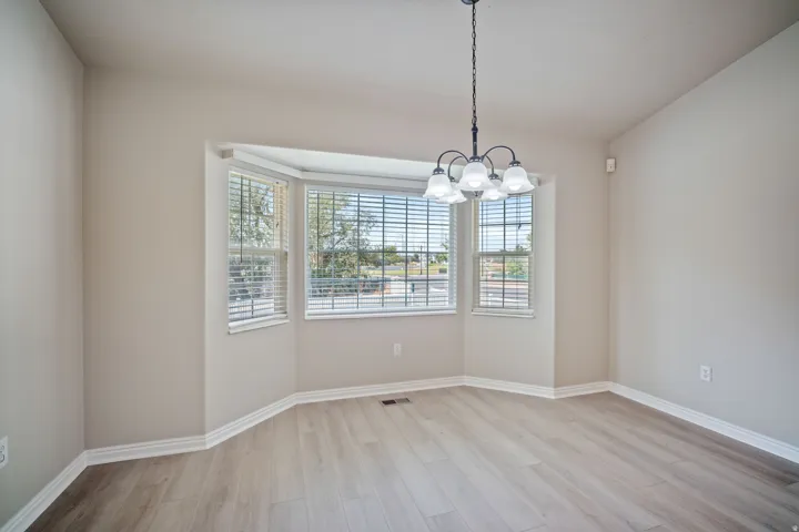 Bay window with blinds, wood-finish flooring, and a five-light chandelier