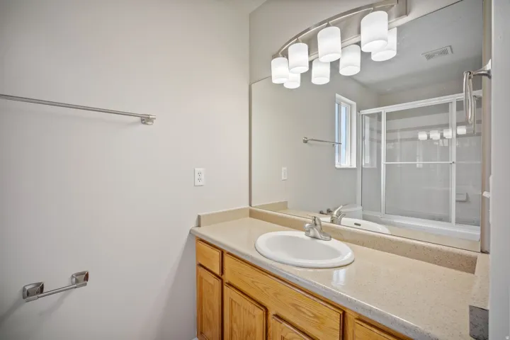 Single vanity with wood cabinetry, integrated sink, and broad mirror
