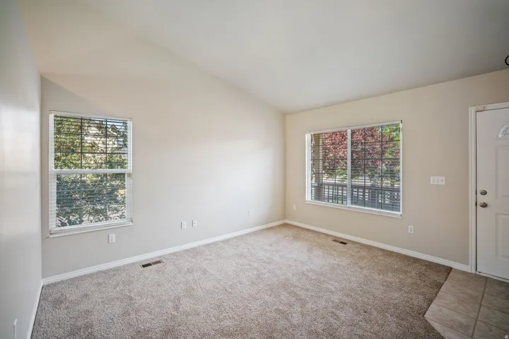 Vaulted ceiling, neutral carpet flooring, two windows, and a white entry door with frosted glass insert
