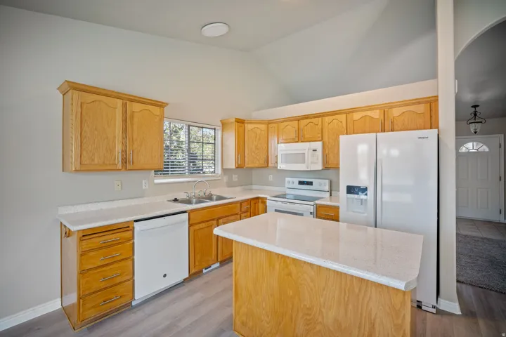 Kitchen featuring light wood cabinetry, light countertops, wood-finish flooring, white appliances, and a vaulted ceiling