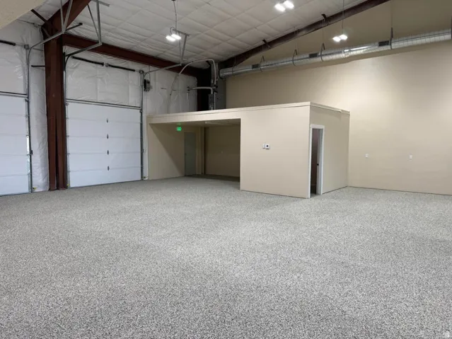 Spacious warehouse interior featuring a newly installed epoxy floor, two large overhead doors, high ceilings with exposed ductwork, and a built-in office or storage area