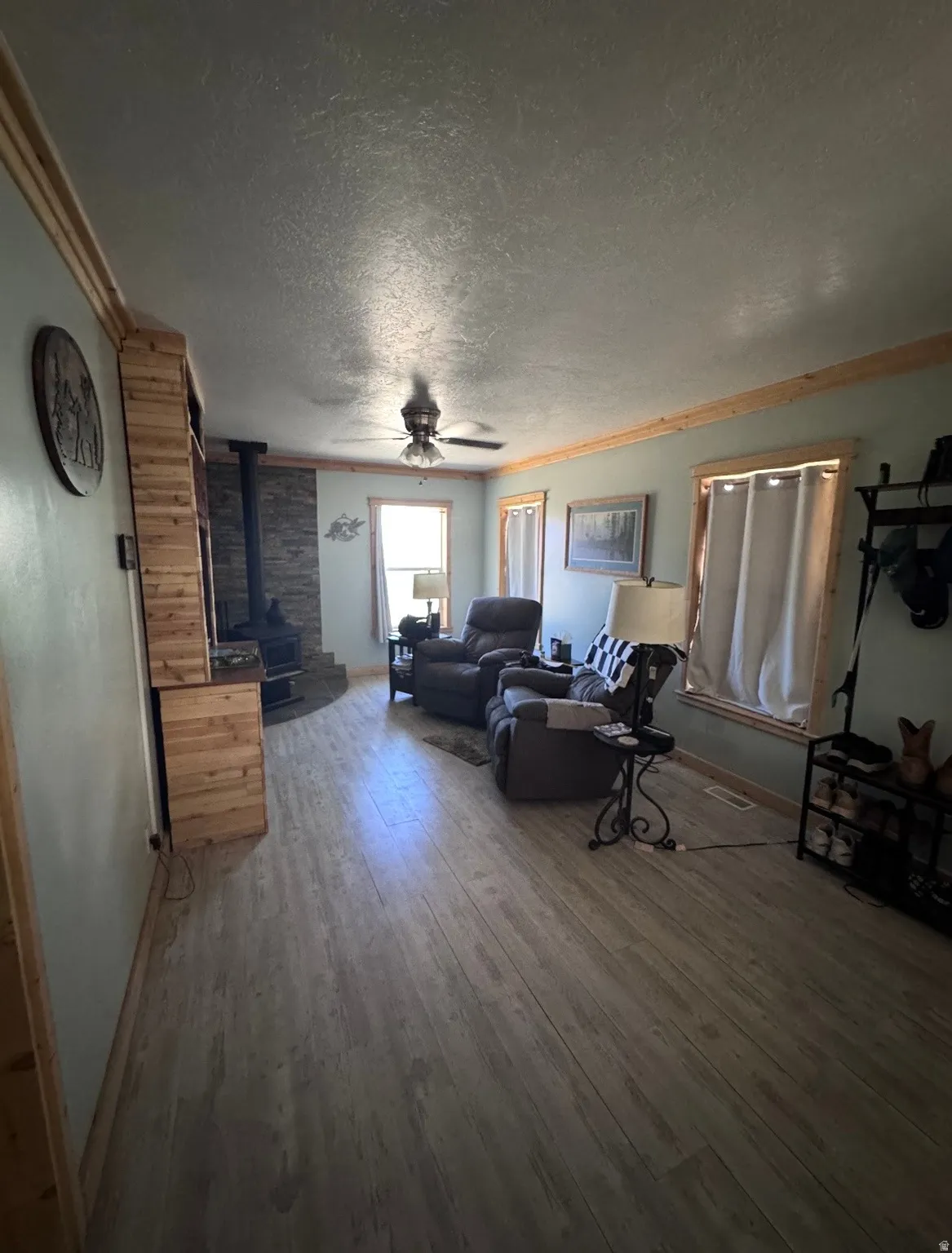 Spacious living area featuring wood-finish flooring, a stone-accented fireplace, and a ceiling fan