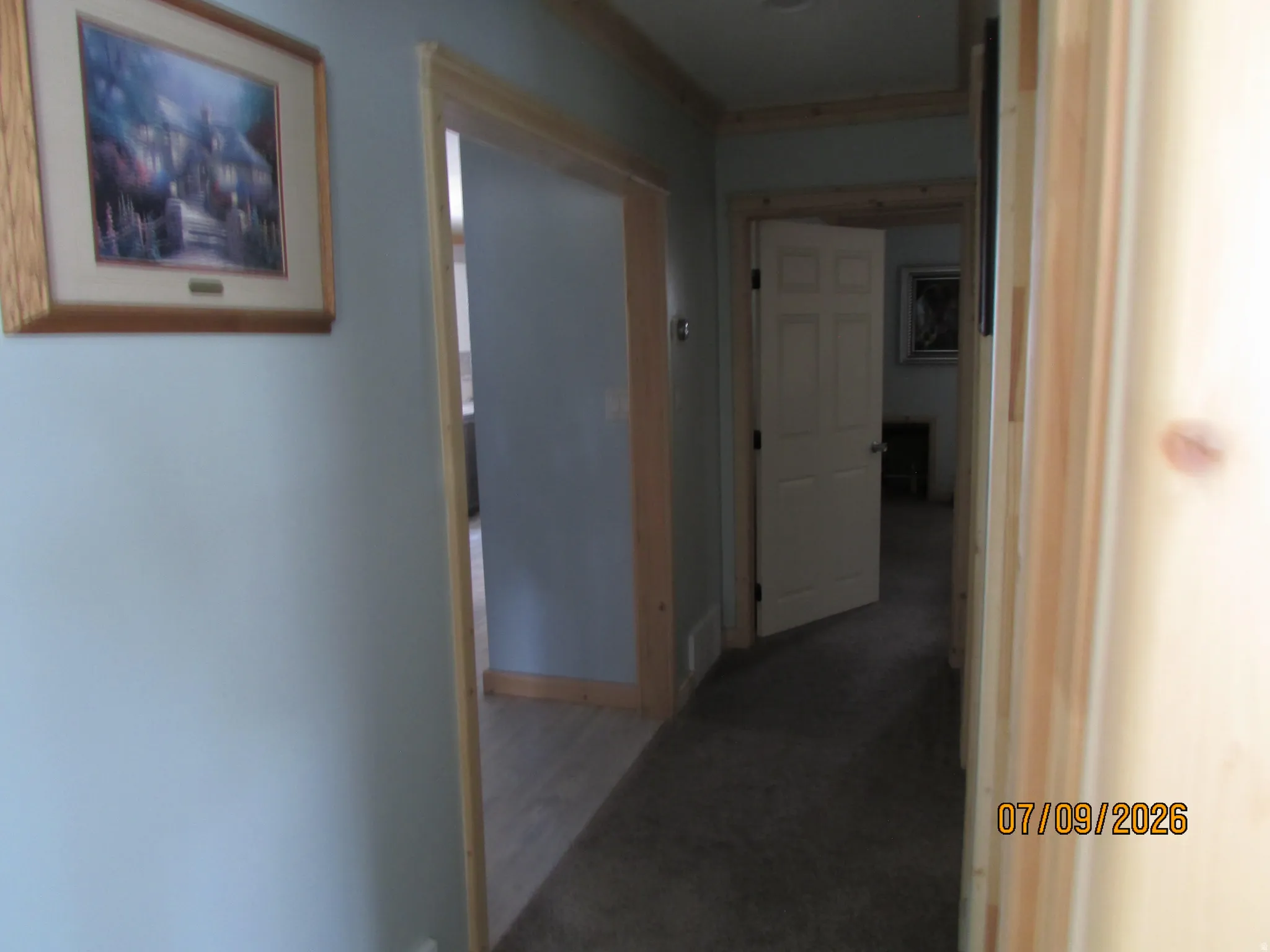 Hallway featuring light blue walls, natural wood trim, and a combination of carpet and wood-finish flooring