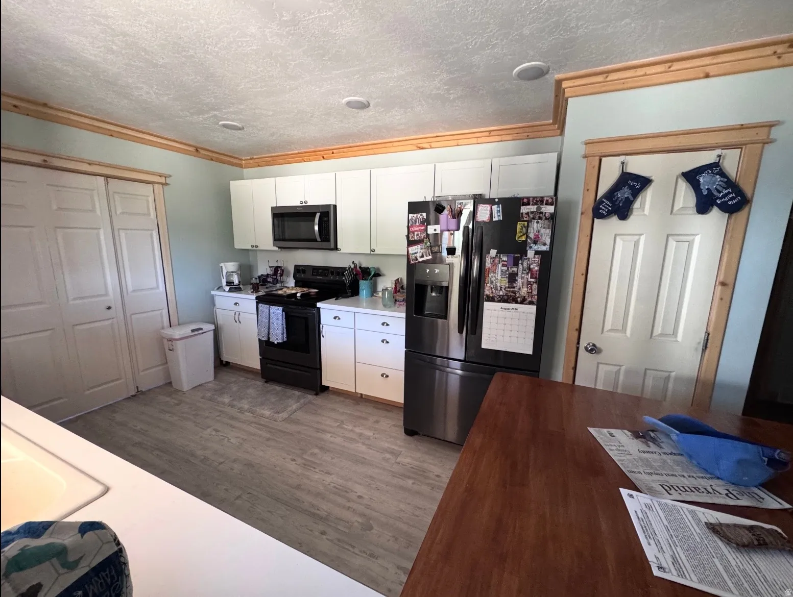 Spacious kitchen featuring white cabinetry, stainless steel appliances including a French-door refrigerator and black range, wood-finish flooring throughout, recessed ceiling lighting, and abundant counter space with a wood-top island for meal preparation