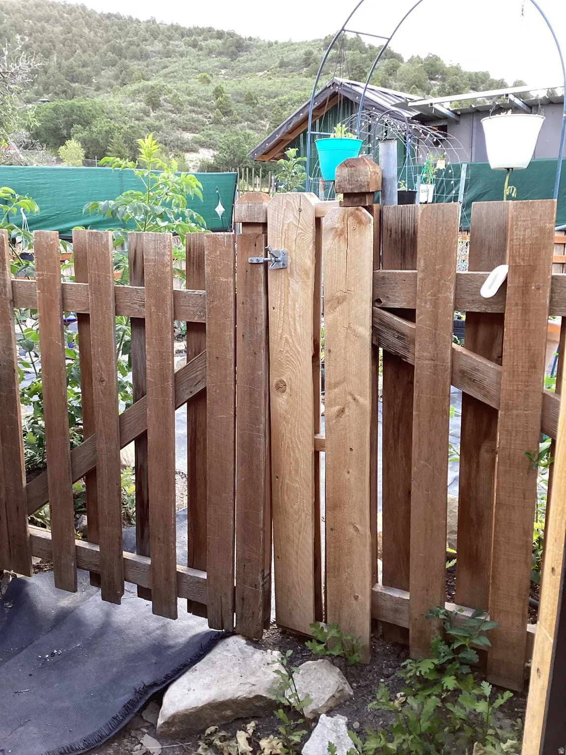 Natural wood fence with a latch gate, set against a backdrop of mature greenery and distant hills