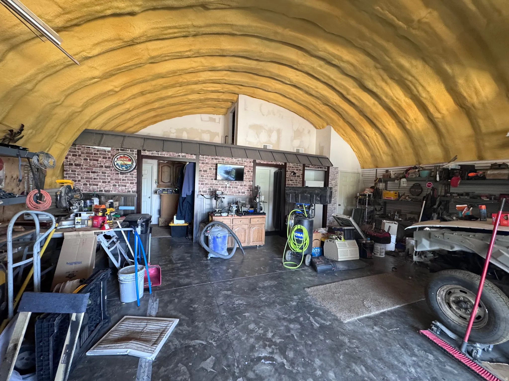 Quonset hut structure featuring an arched, insulated ceiling, a durable concrete floor, and interior brick-finish walls