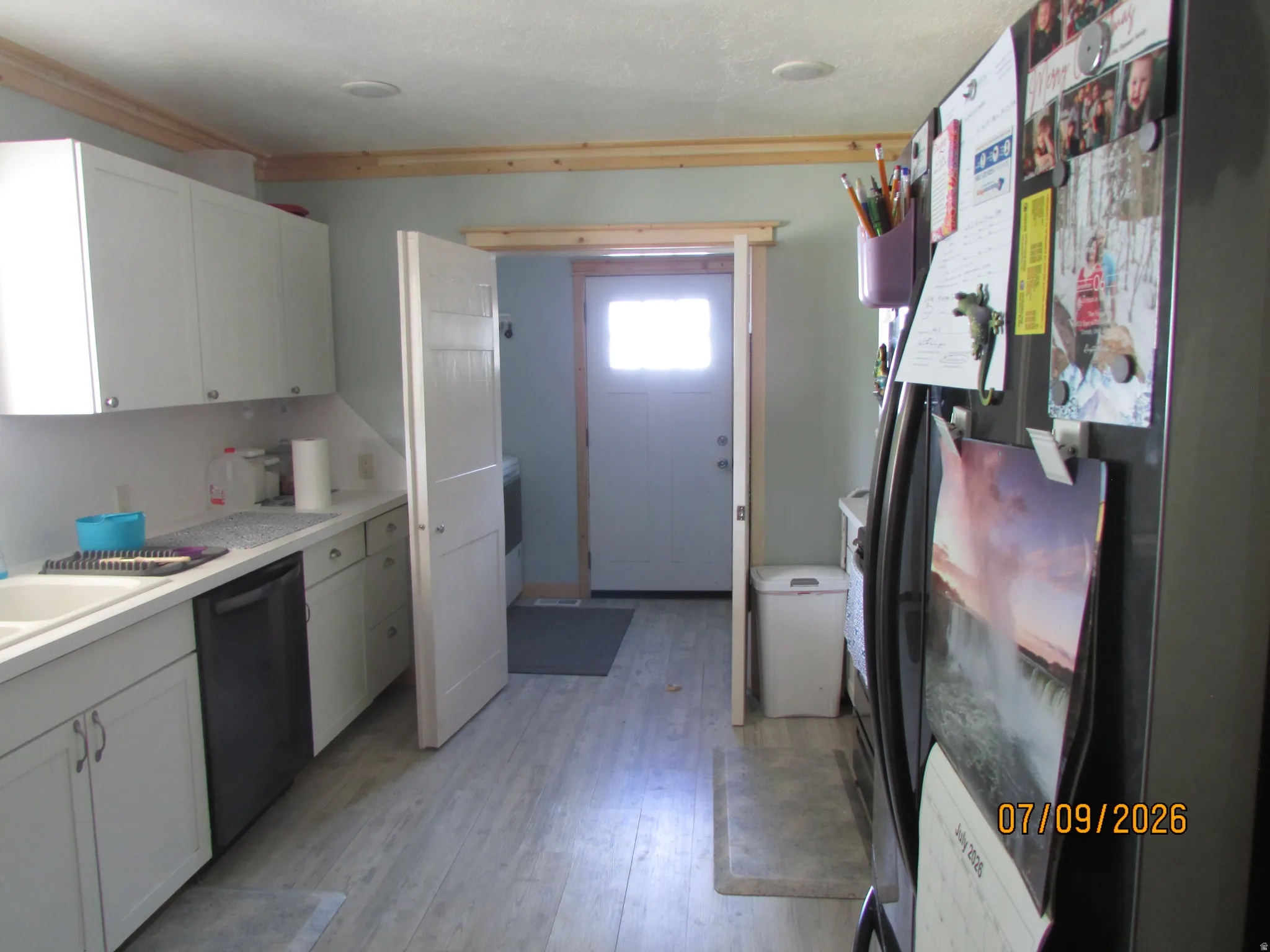 Galley kitchen featuring white cabinetry, light countertops, wood-finish flooring, and a stainless steel refrigerator
