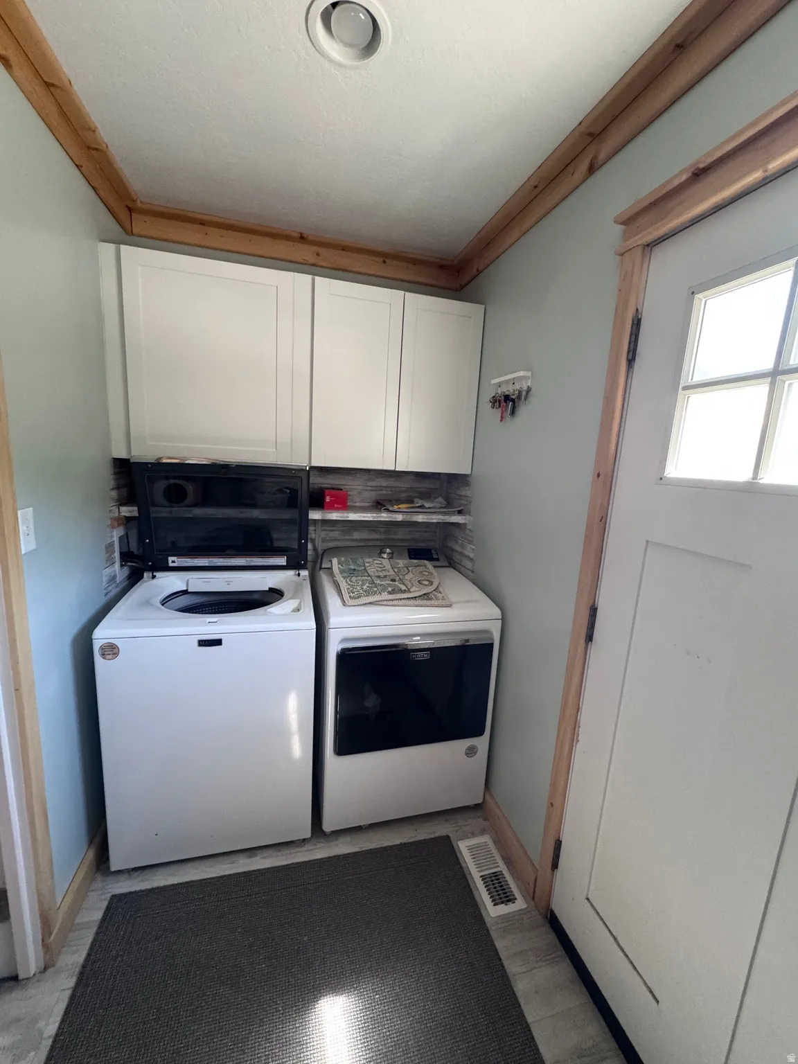 Dedicated laundry room featuring a full-size top-load washer and front-load electric dryer, white cabinetry with ample storage, wood-trimmed ceiling detail, and dark tile flooring for durability and easy maintenance