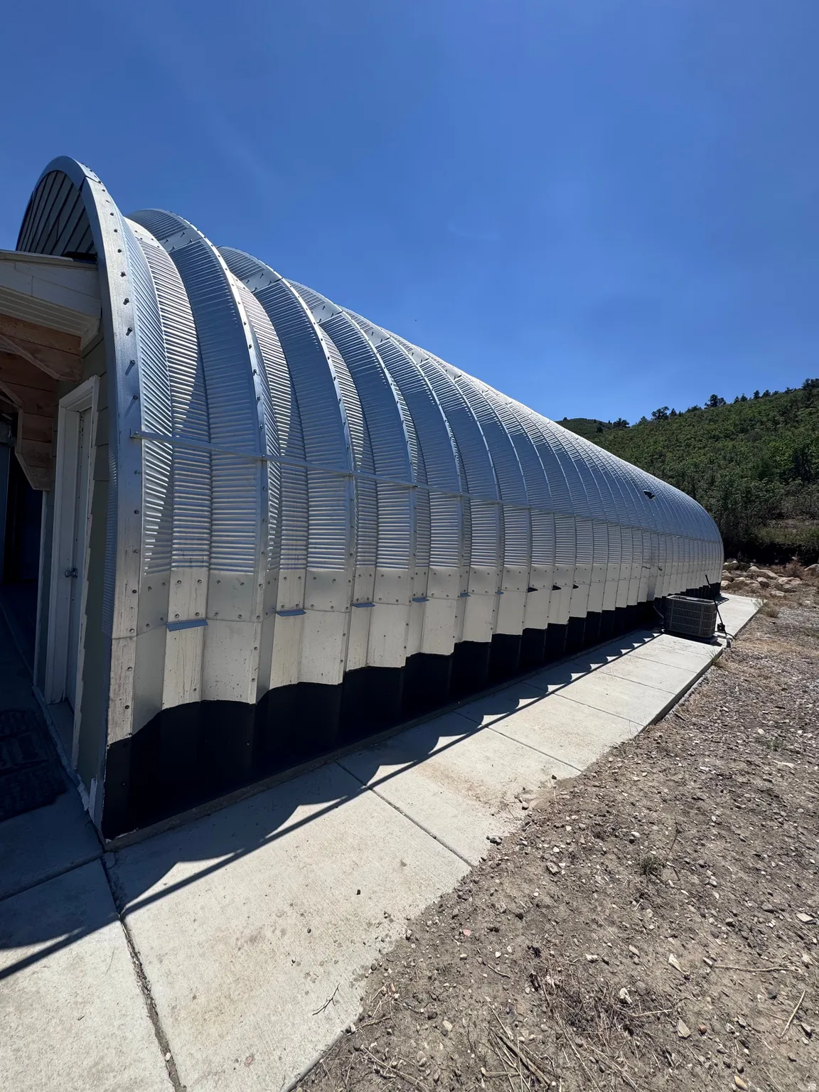 Modern metal agricultural or commercial storage structure featuring a distinctive curved corrugated metal roof with vertical ribbed paneling, durable steel construction, and a concrete foundation pad