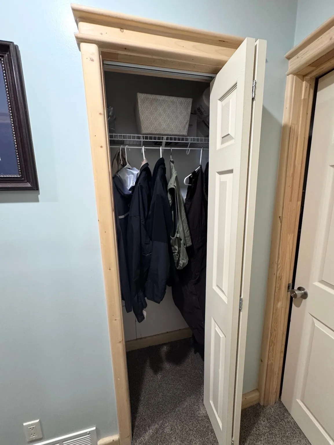 Interior closet featuring a bi-fold door, natural wood trim, light blue wall paint, wire shelving, and grey carpet flooring