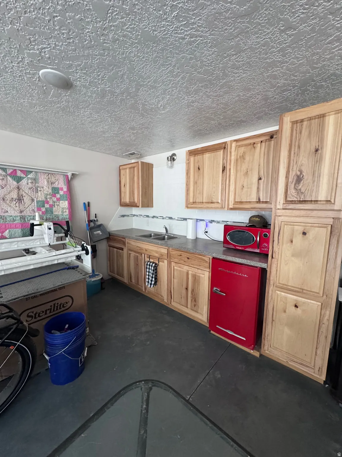 Kitchenette area featuring wood-finish cabinetry, a stainless steel sink, and a gray countertop