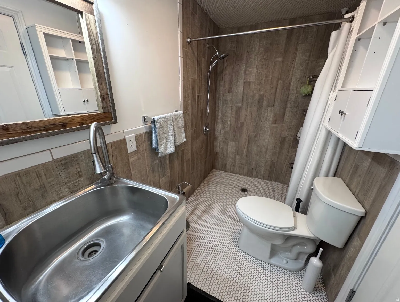 Bathroom featuring a walk-in shower with wood-finish tile surround, hexagon mosaic floor tiling, and a wall-mounted showerhead