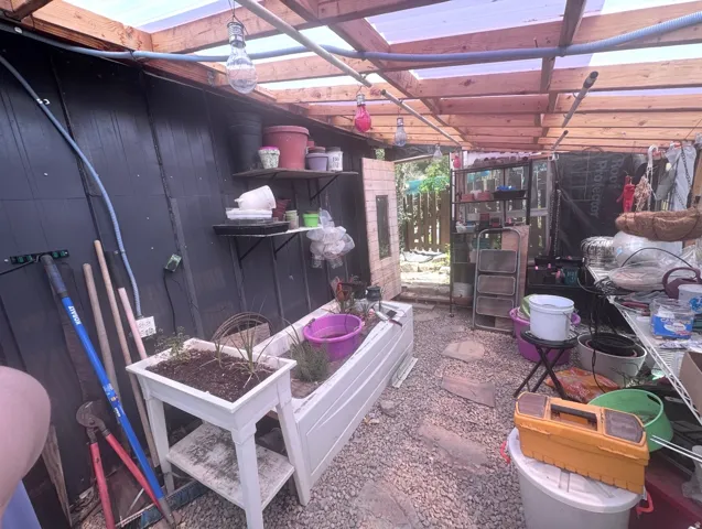 Greenhouse structure featuring a wood frame, translucent panel roof, and gravel flooring