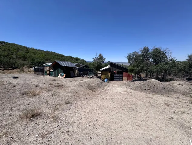 Expansive open land featuring two structures with metal roofing and various exterior finishes, surrounded by natural vegetation and distant hills