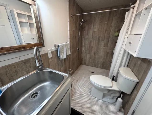 Bathroom featuring a walk-in shower with wood-finish tile surround, hexagon mosaic floor tiling, and a wall-mounted showerhead