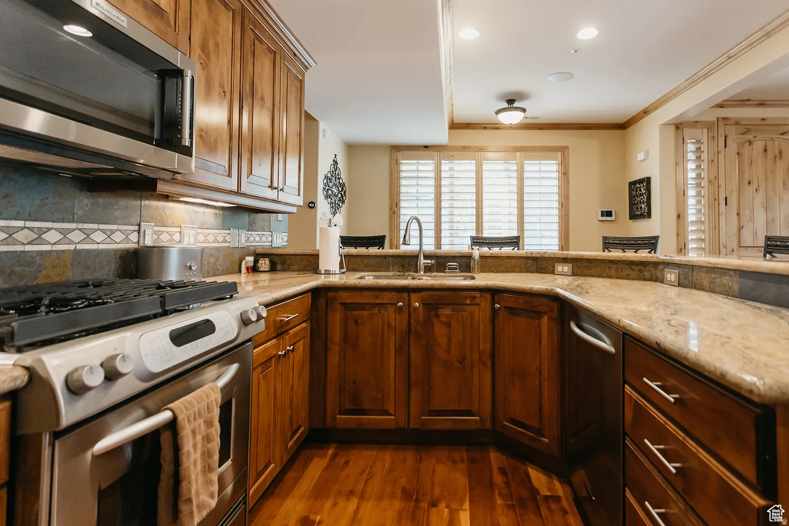 Kitchen featuring a stainless steel range and microwave, wood-finish flooring, stone countertops, and wood cabinetry