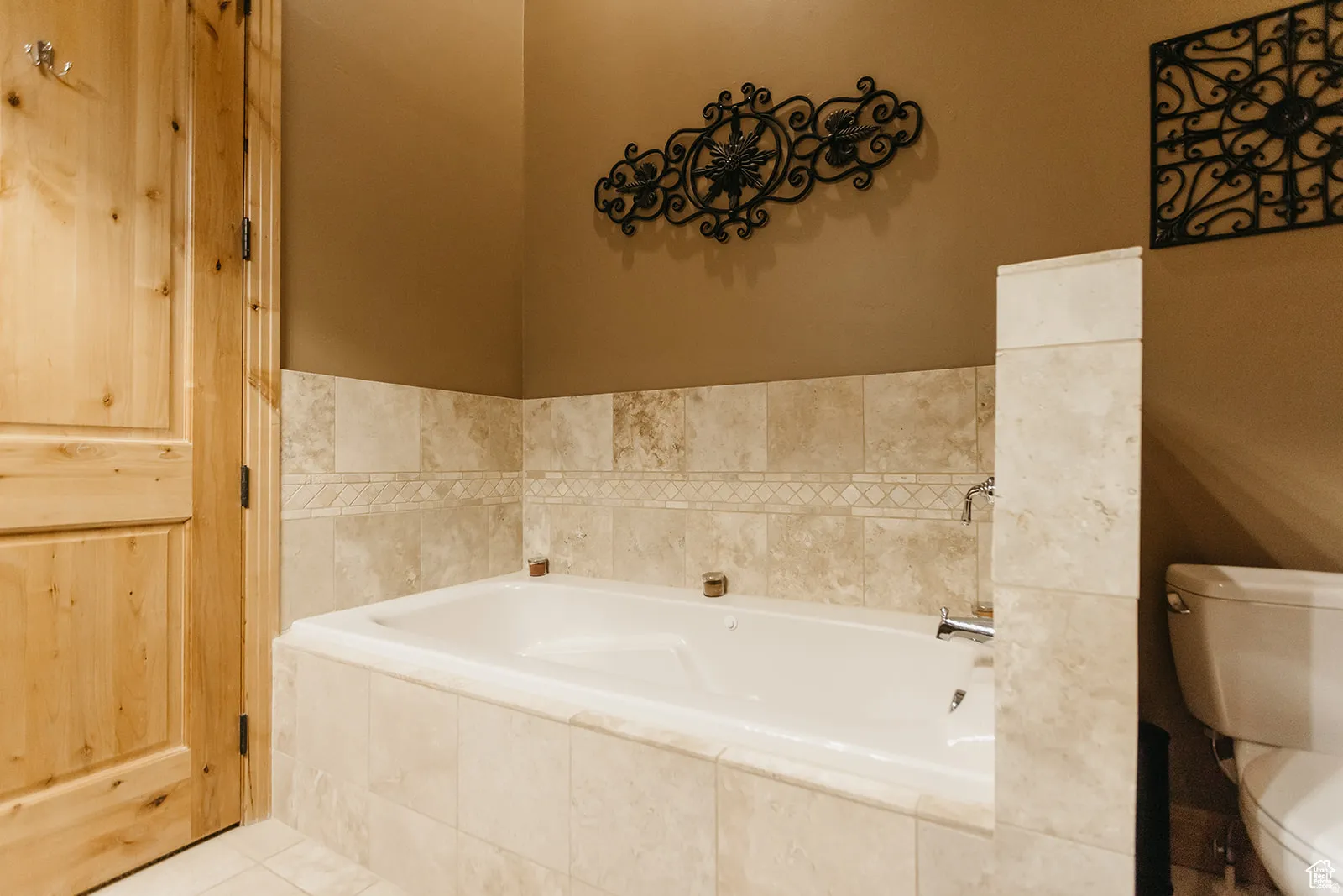 Built-in soaking tub with tile surround, decorative tile accent band, and chrome fixtures