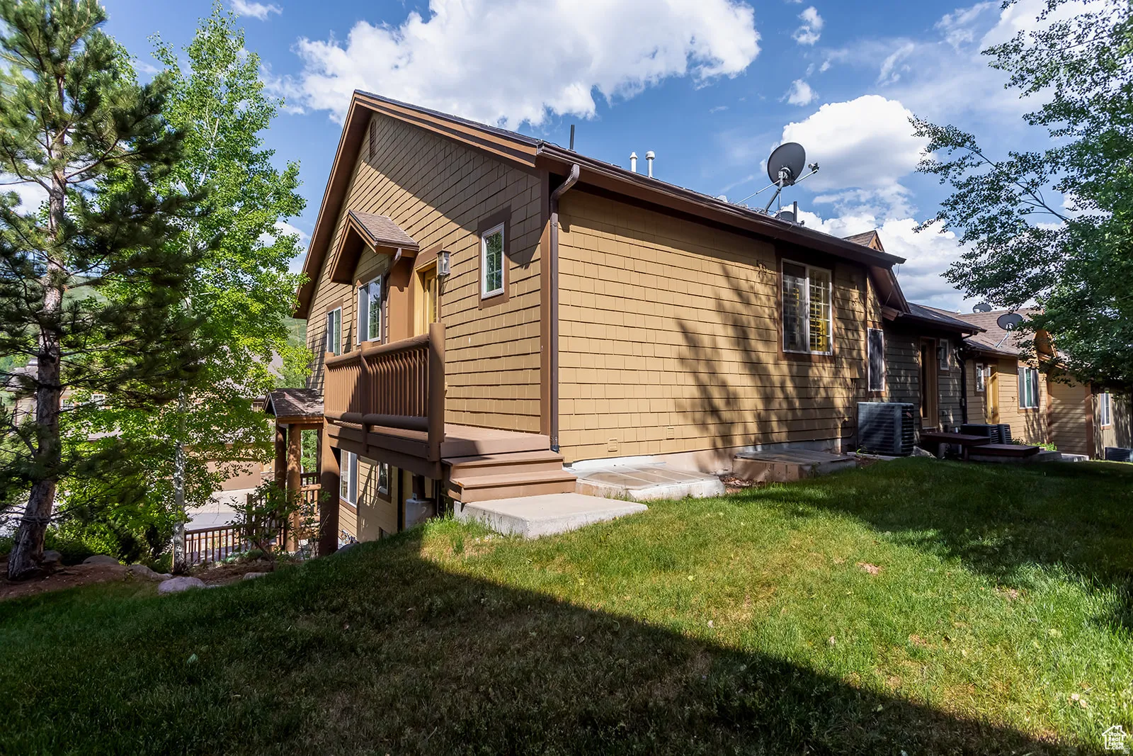 Exterior featuring tan shingle siding, brown trim, a covered entry with a railing, and multiple windows