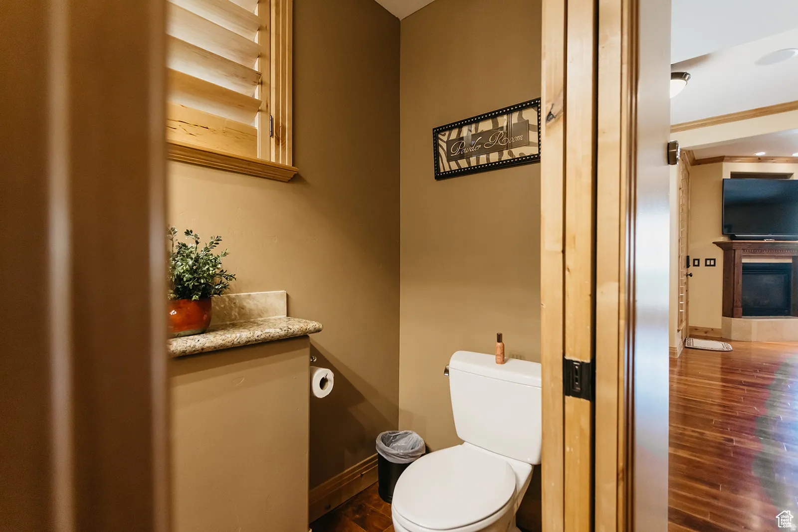 Powder room featuring a granite-style countertop, wood-finish flooring, and a window with wood louvered shutters