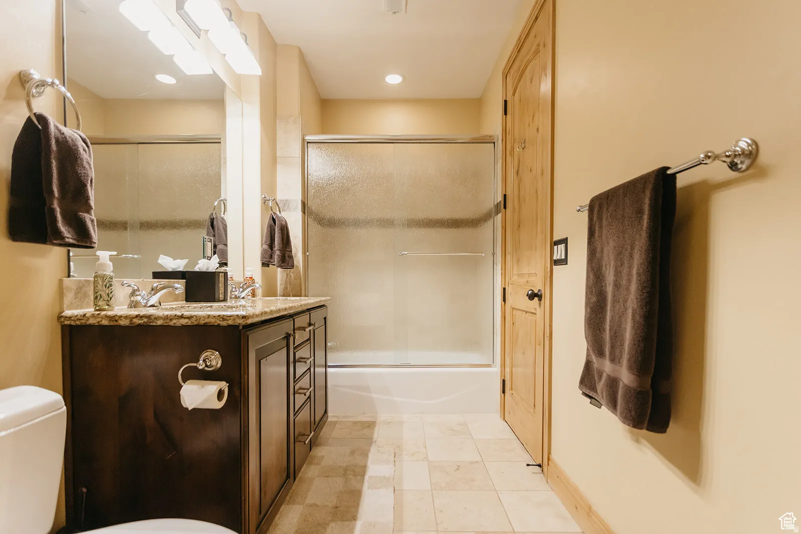 Bathroom featuring a dark wood vanity with a granite countertop, a double sink with chrome fixtures, and a shower-tub combination with a sliding glass door