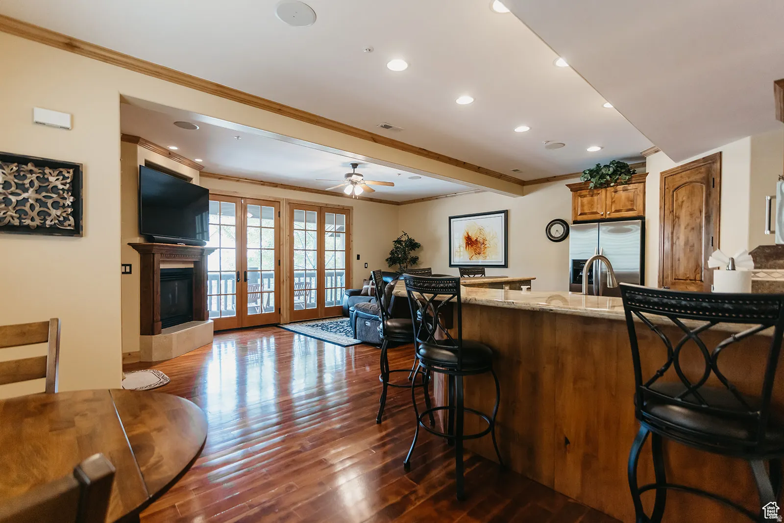 Open-concept living space featuring wood-finish flooring, a kitchen island with stone countertop, and an integrated fireplace with wood mantle
