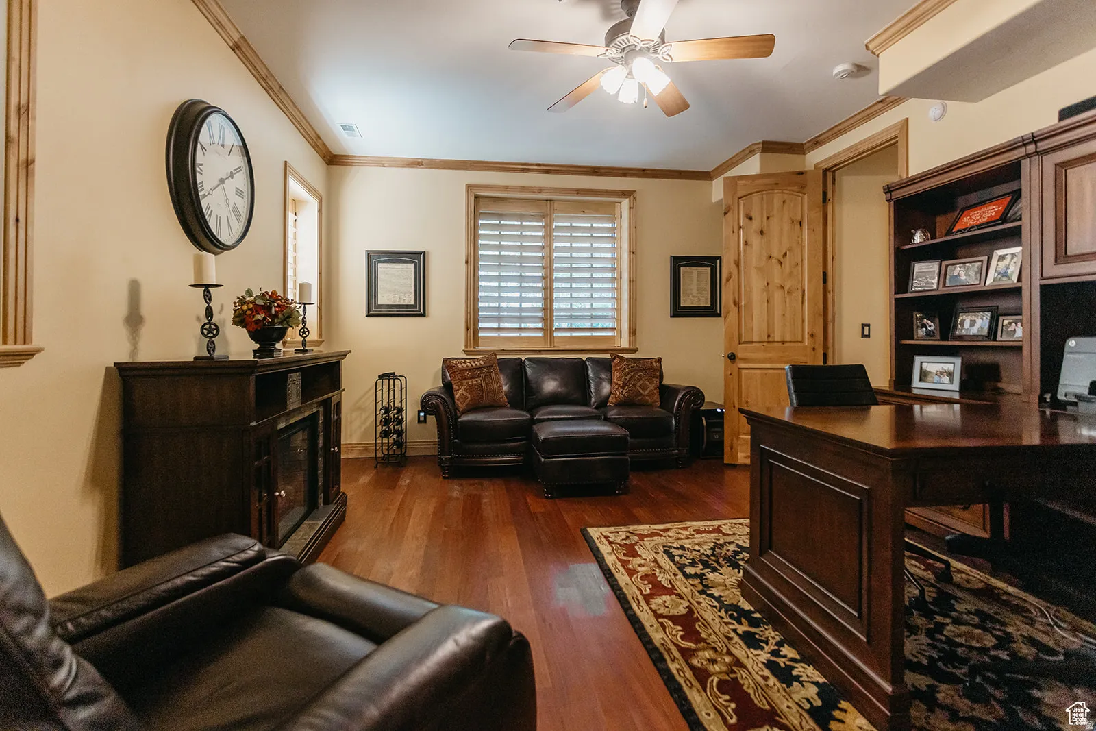 Spacious interior featuring wood-finish flooring, a built-in fireplace console, a ceiling fan with integrated lighting, window shutters, and a built-in shelving unit