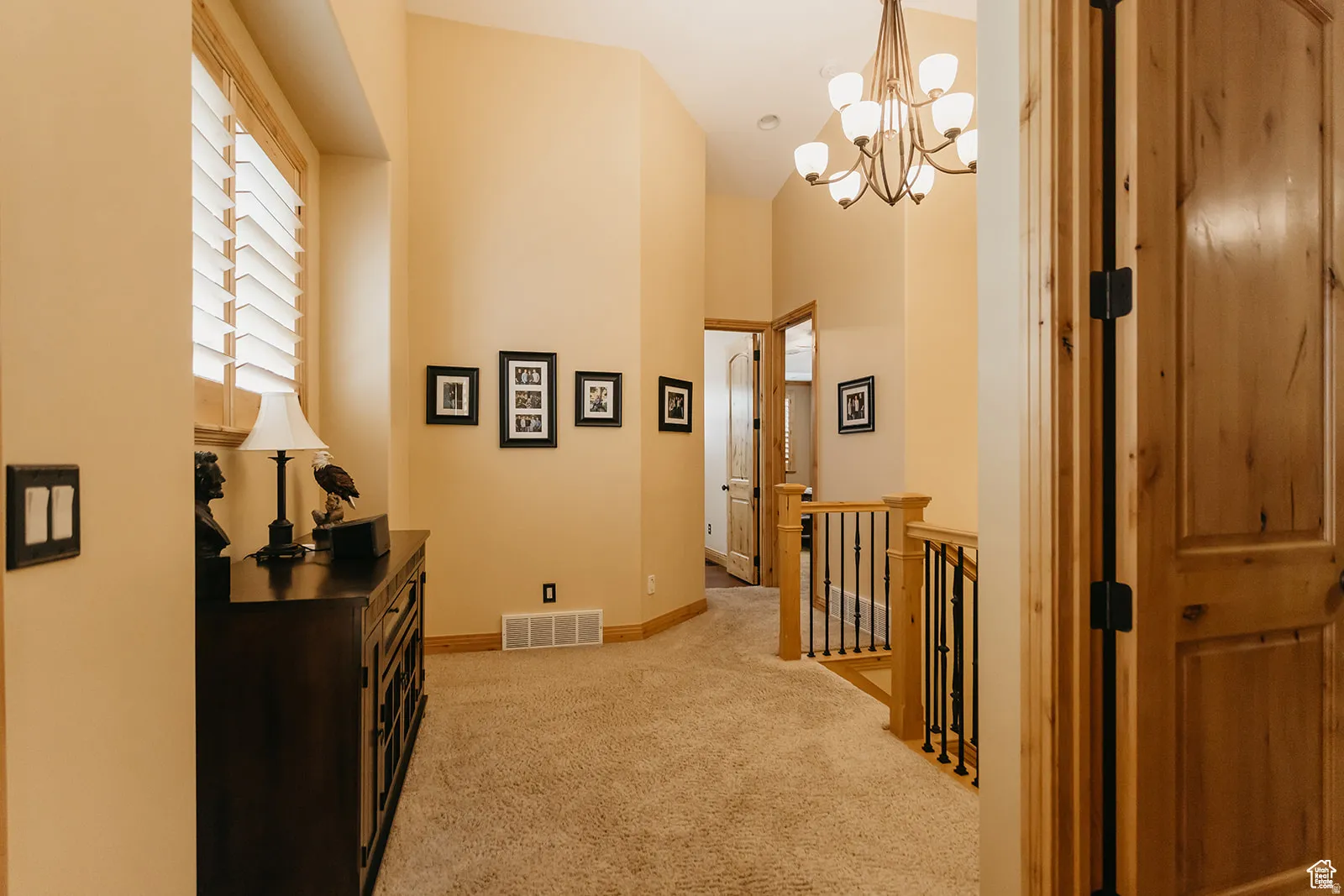 Carpeted corridor with wood trim, plantation shutters, and a multi-bulb chandelier