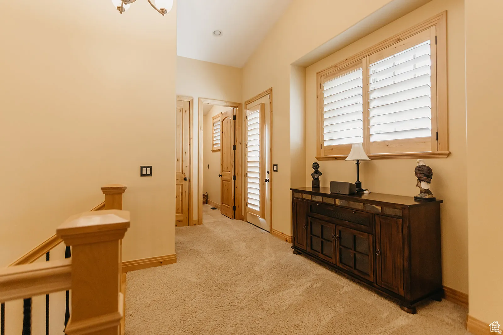 Second-story landing featuring a window with natural wood plantation shutters, light beige carpeting, and natural wood baseboards
