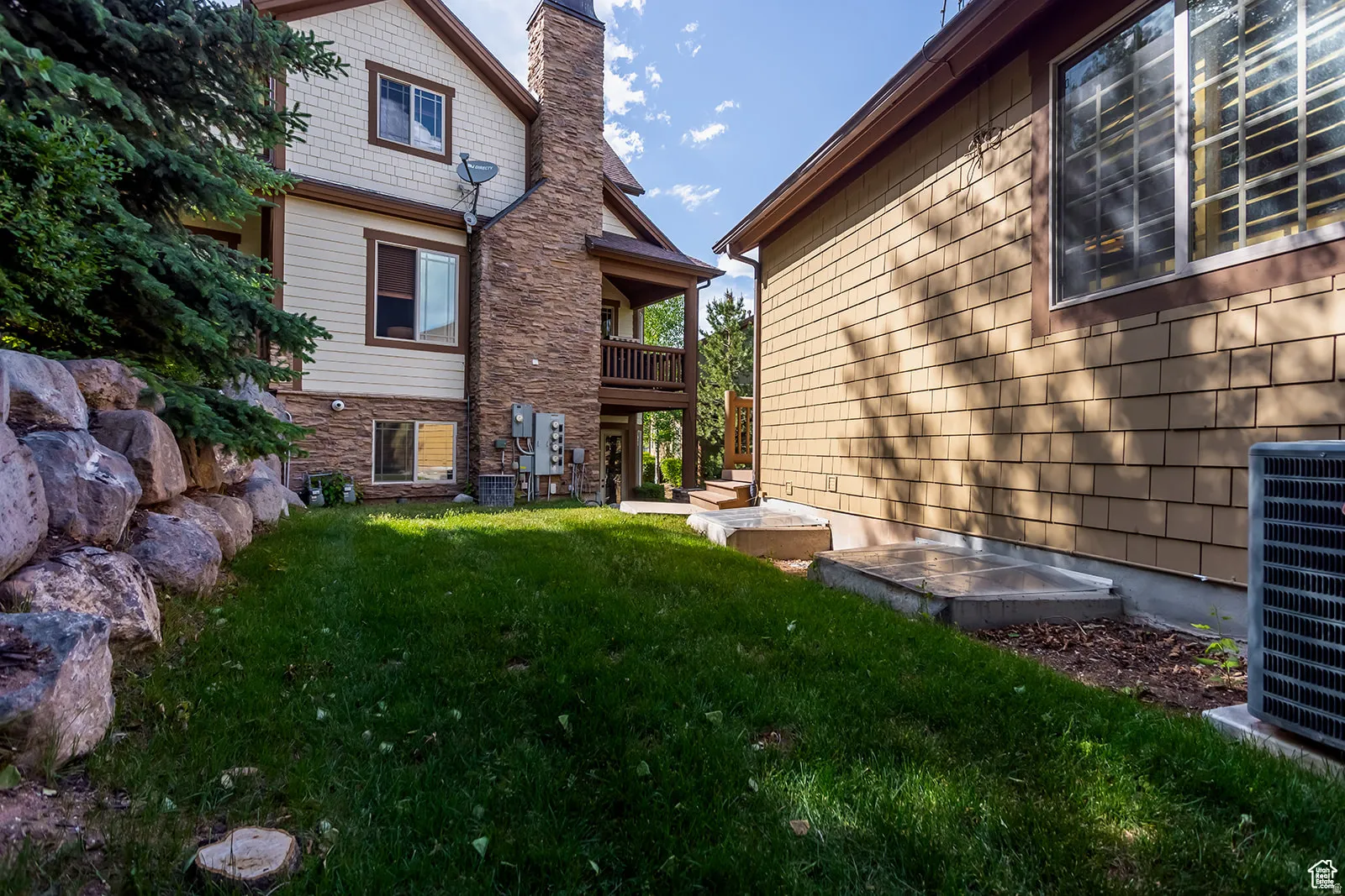 Rear exterior featuring a stone chimney, upper-level balcony, and wood siding