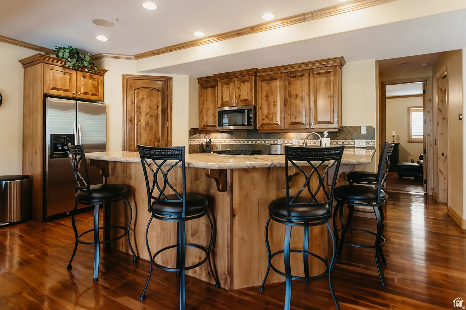 Kitchen featuring wood-finish cabinetry, stainless steel appliances, recessed lighting, and a breakfast bar with stone countertops and a tiled backsplash