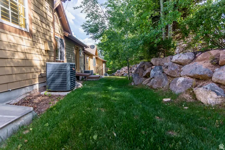 Manicured lawn area bordered by a natural stone retaining wall, mature trees, and a tan shingle-sided exterior