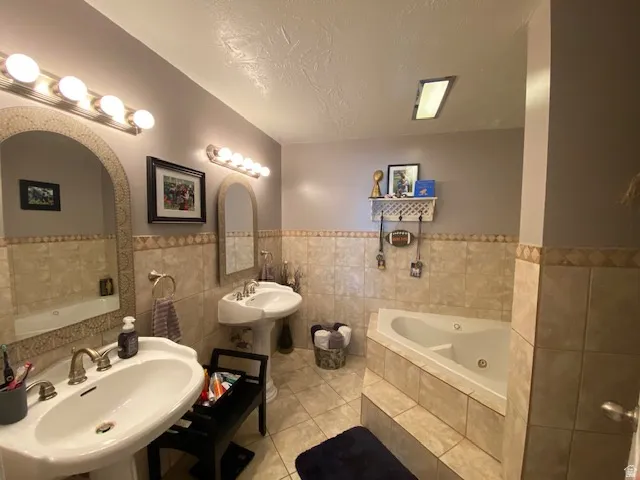 Bathroom featuring dual pedestal sinks with brass-finish fixtures, a tiled soaking tub, and floor-to-ceiling tile