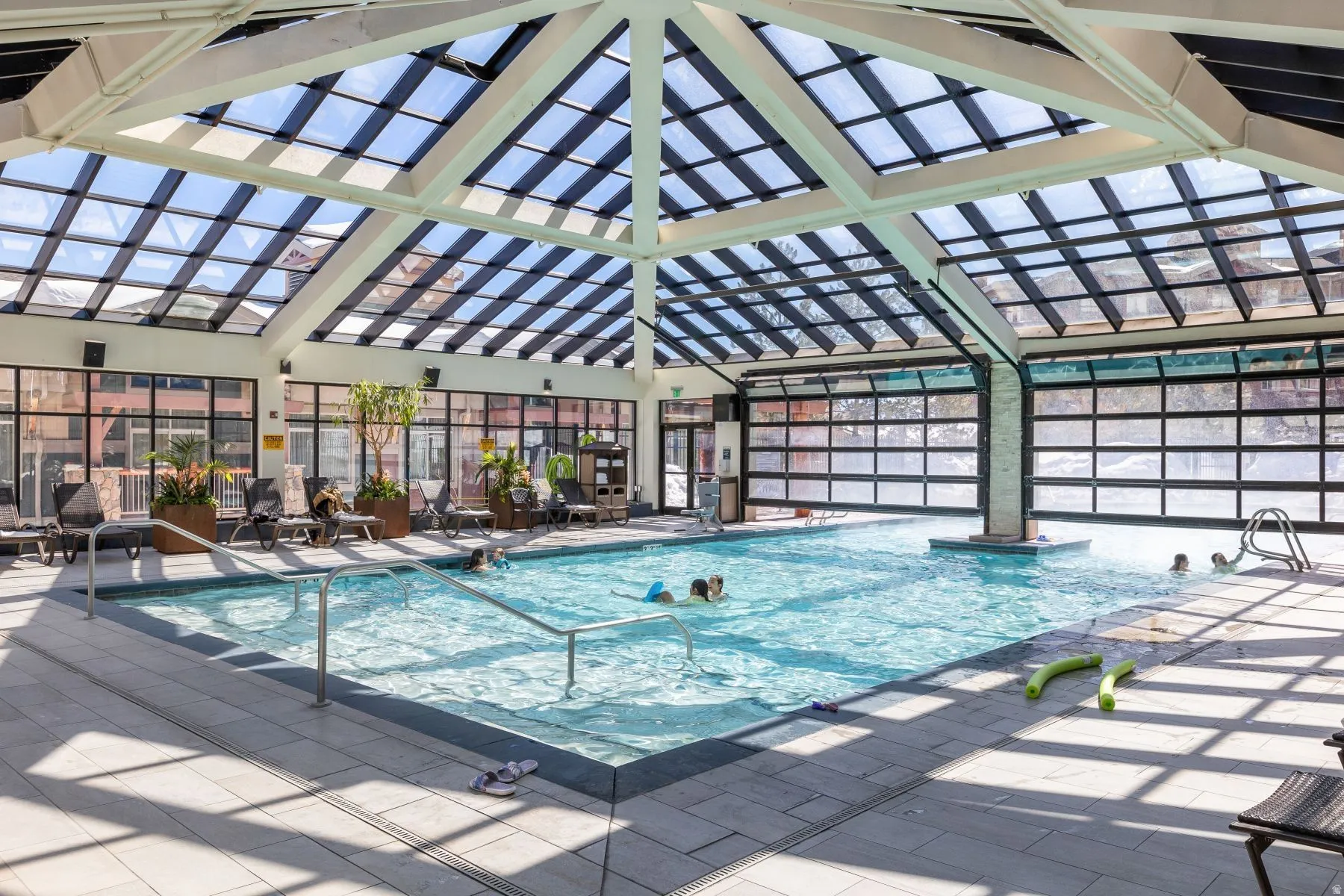 Indoor swimming pool featuring a glass-paneled ceiling, expansive window walls, and tiled flooring
