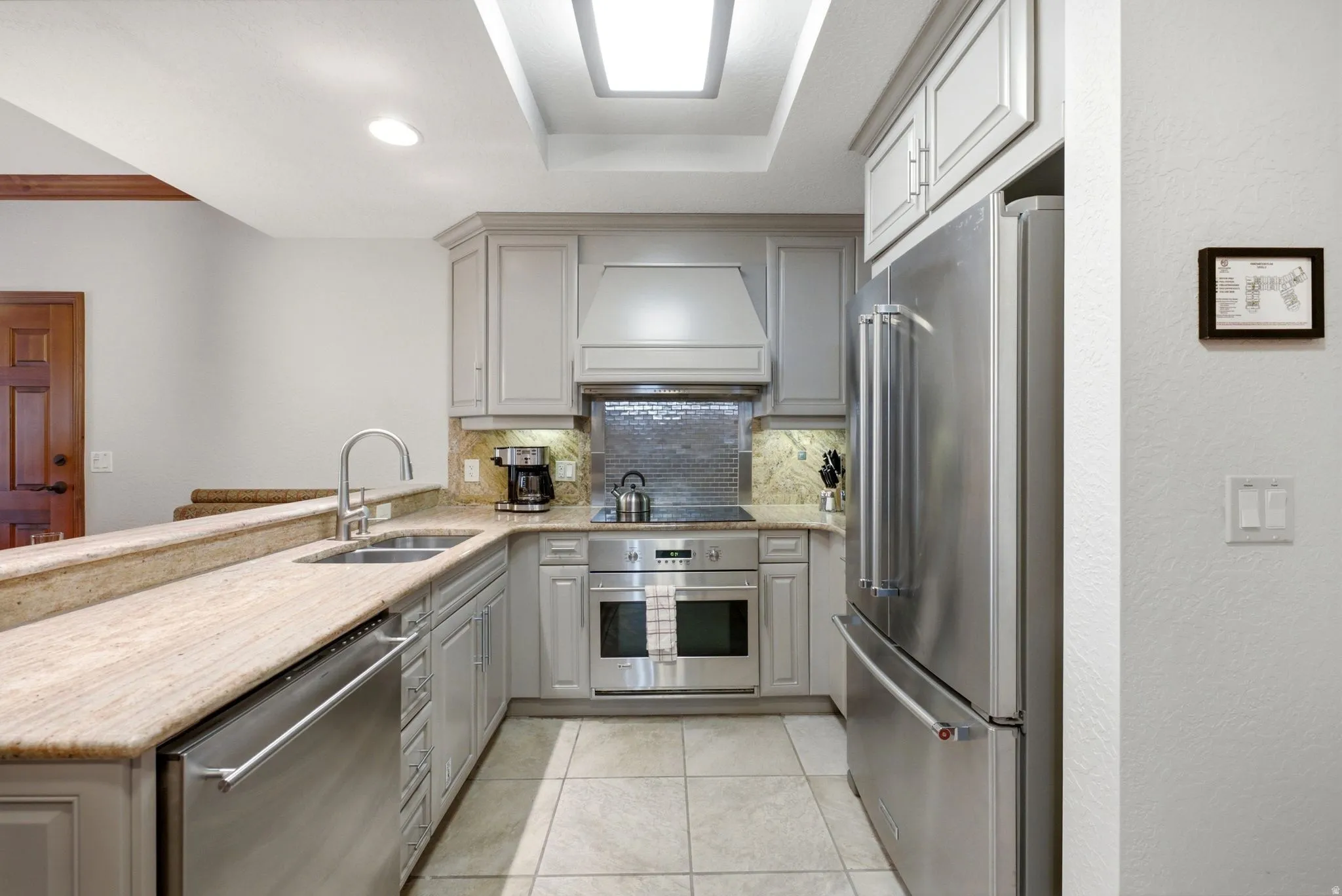 Contemporary kitchen featuring stainless steel appliances, light wood-finish cabinetry, and a textured backsplash