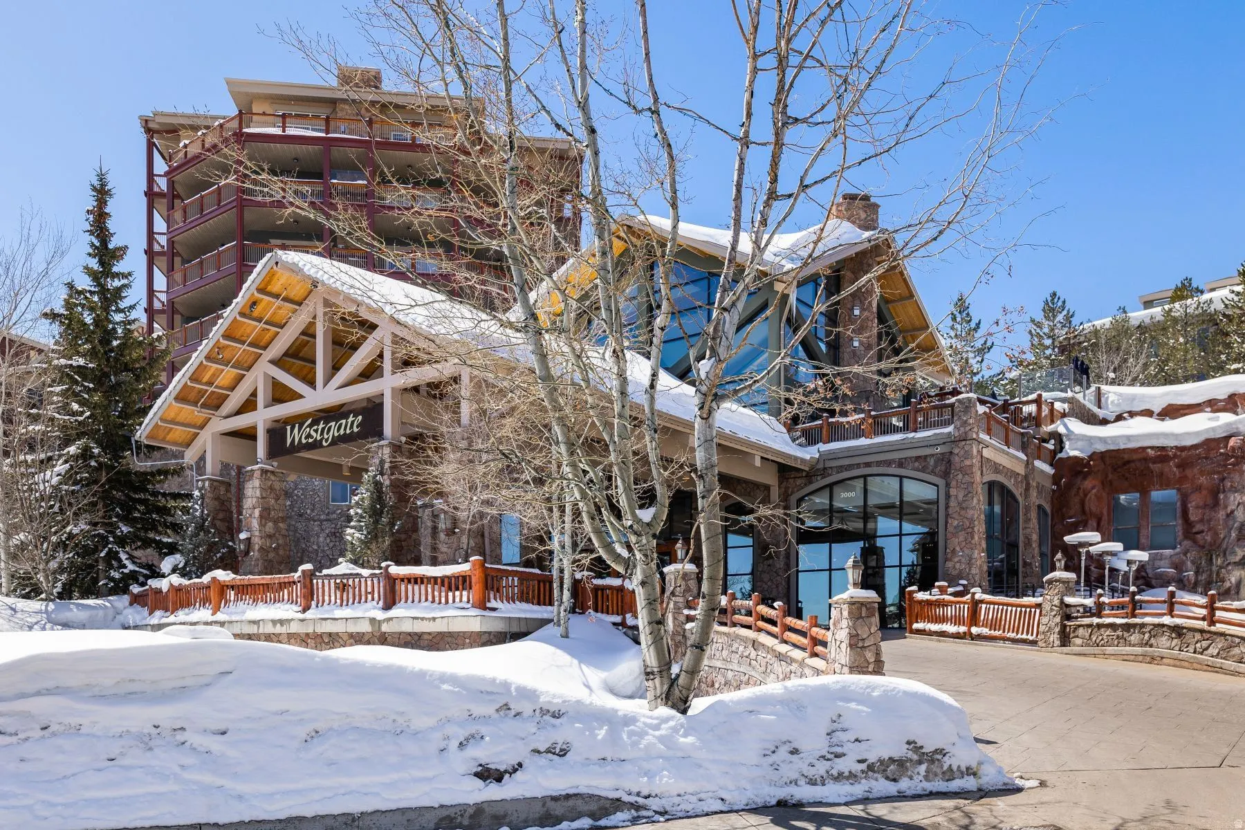 Stone and timber exterior featuring a porte-cochère entrance, extensive glazing, and multiple levels of balconies