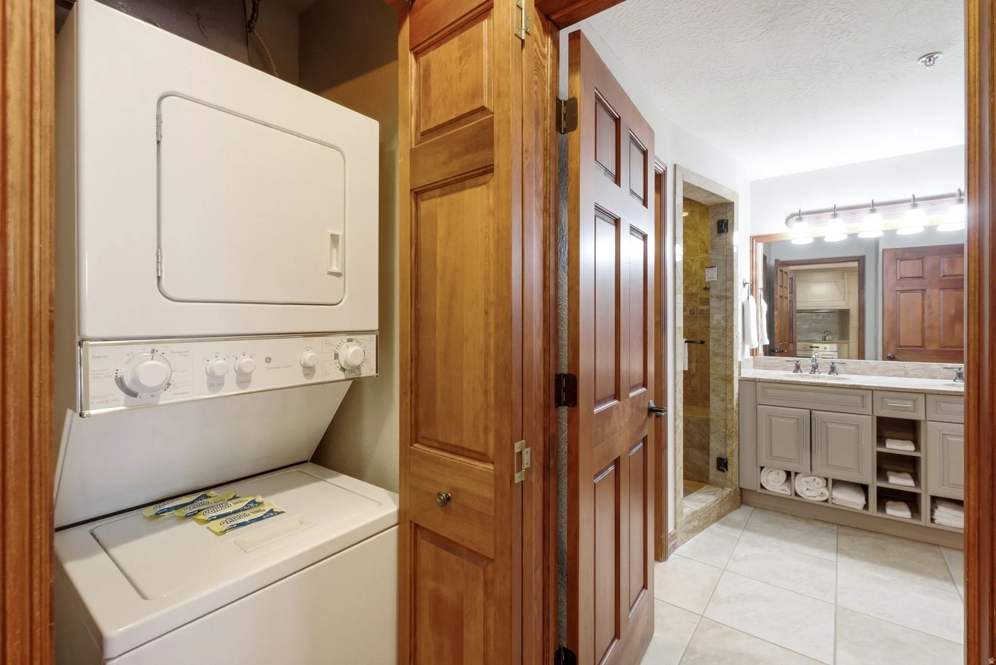 Stacked washer and dryer unit within a dedicated laundry closet featuring natural wood doors