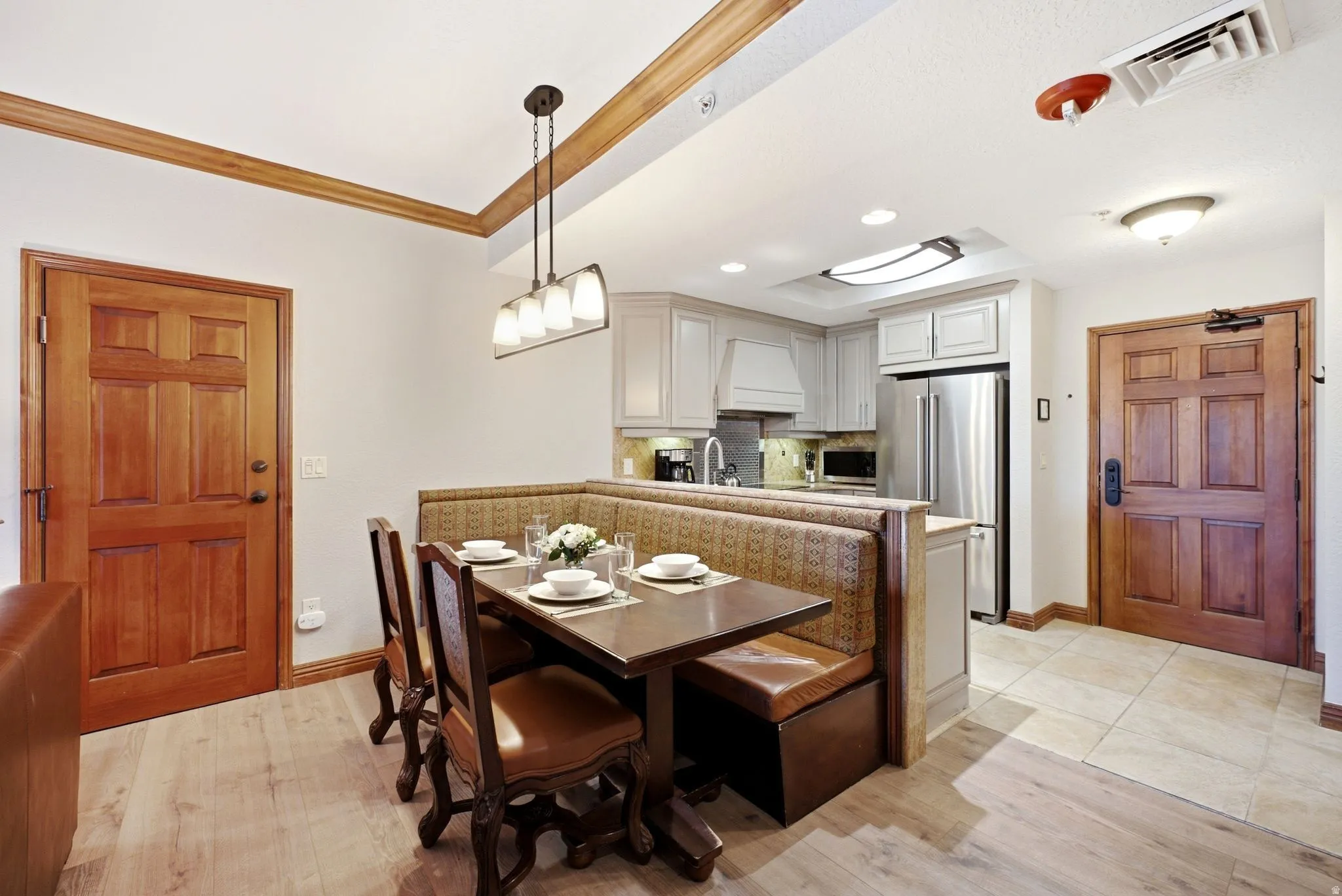 Open-concept kitchen and dining area featuring light wood-finish flooring, a built-in banquette, light-toned cabinetry, and stainless steel appliances