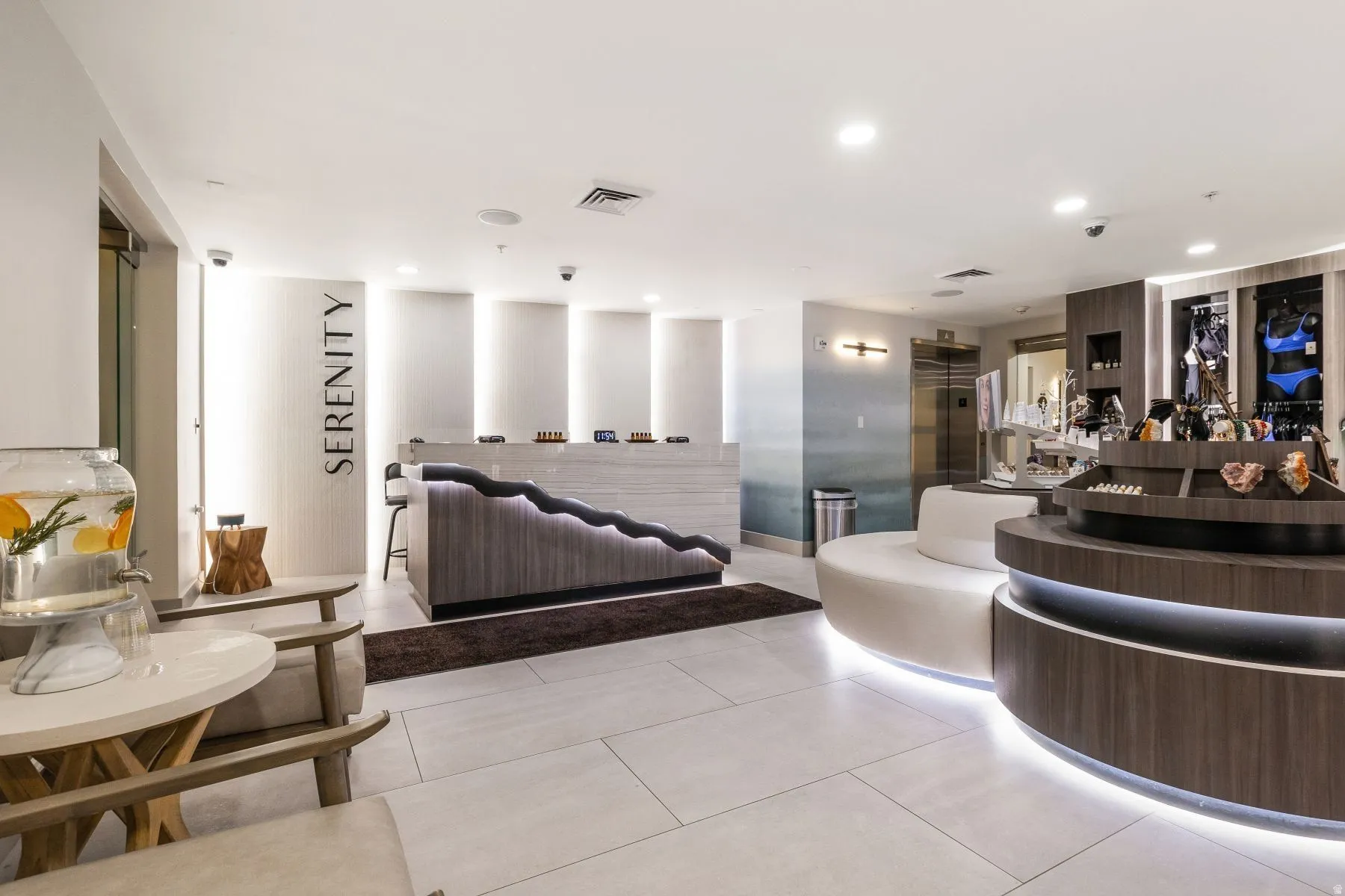 Modern reception area featuring light-toned large format floor tiles, integrated ceiling lighting, and a wood-finish reception desk with accent lighting