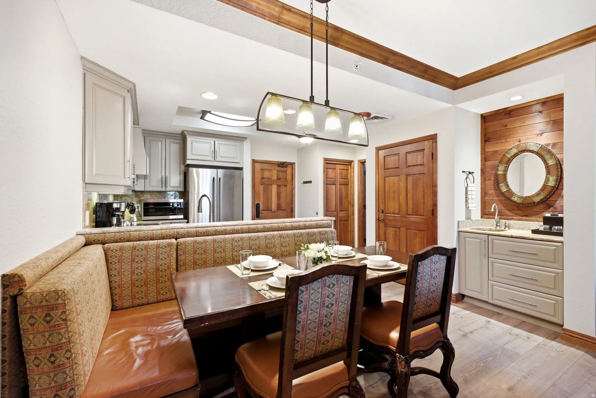Open-concept dining area featuring a built-in banquette, wood-finish flooring, a contemporary chandelier, a wet bar with shaker-style cabinetry, and a kitchen with stainless steel appliances