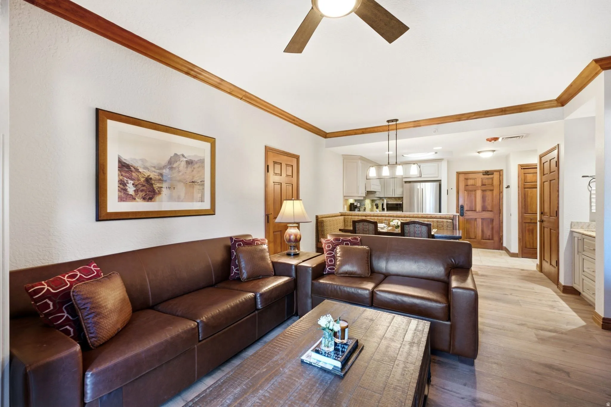 Open-concept living space with wood-finish flooring, crown molding, and a ceiling fan