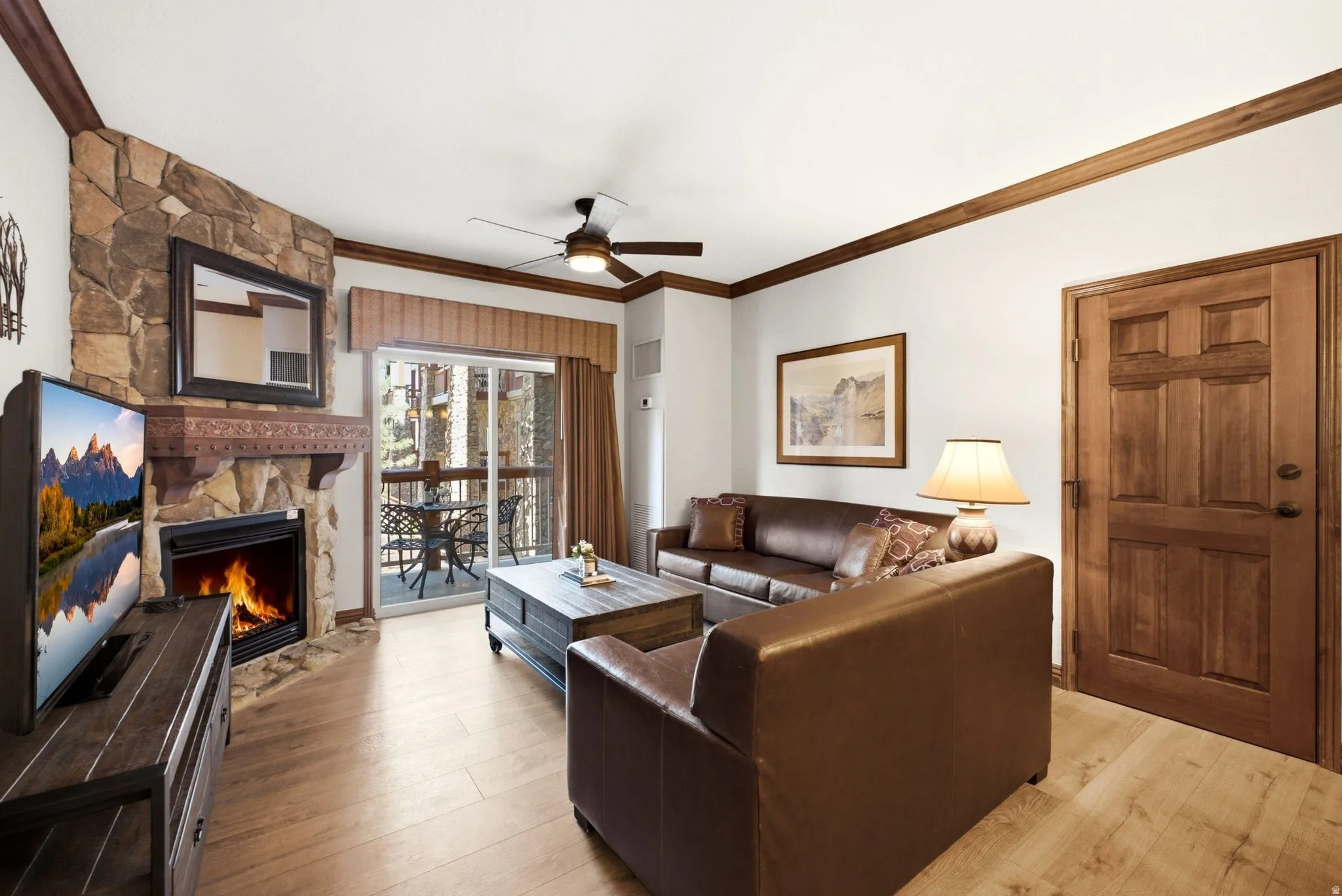 Living area featuring a stone-clad fireplace, wood-finish flooring, and crown molding