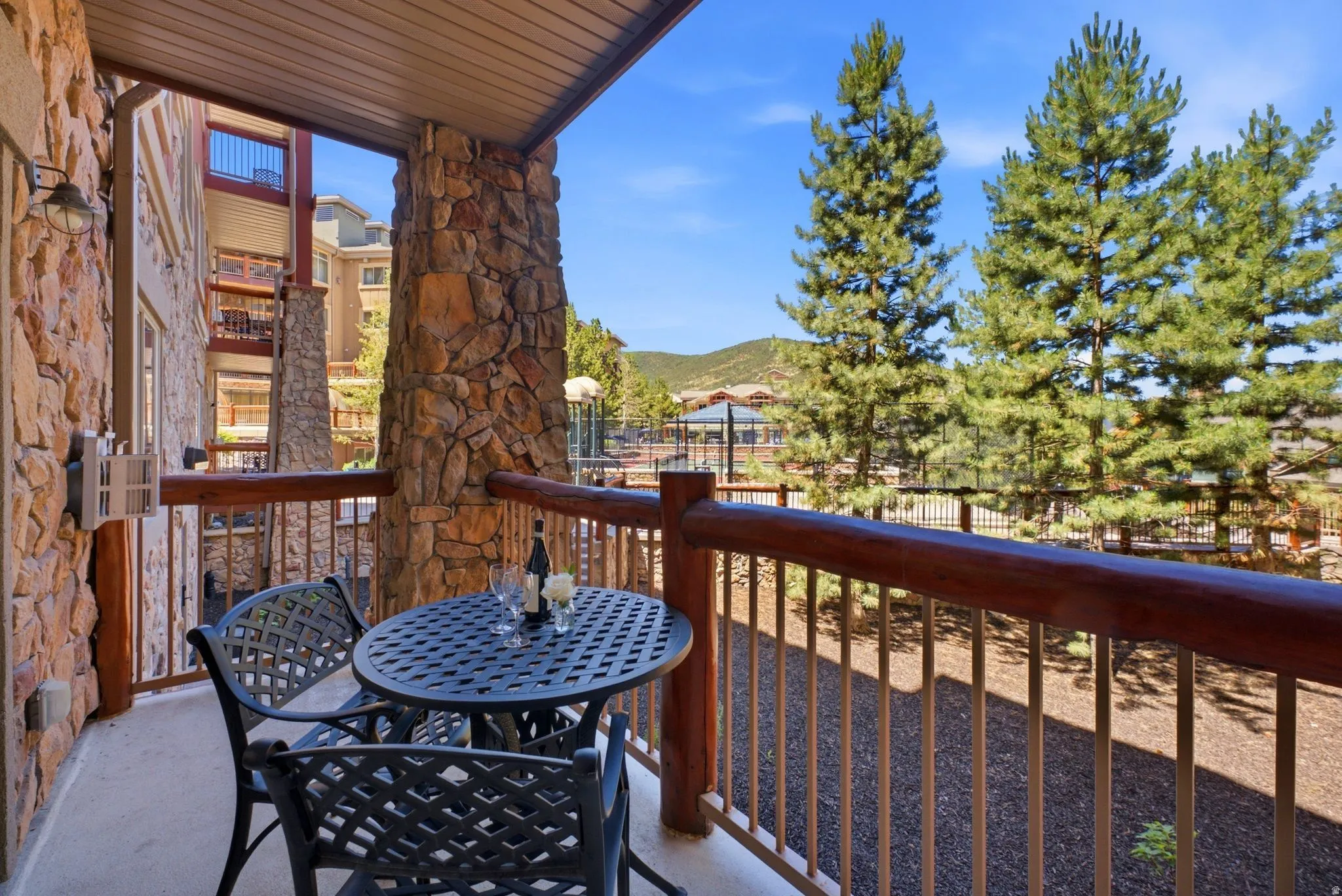 Outdoor patio featuring stone facade, wood-finish railing, and surrounding evergreen trees