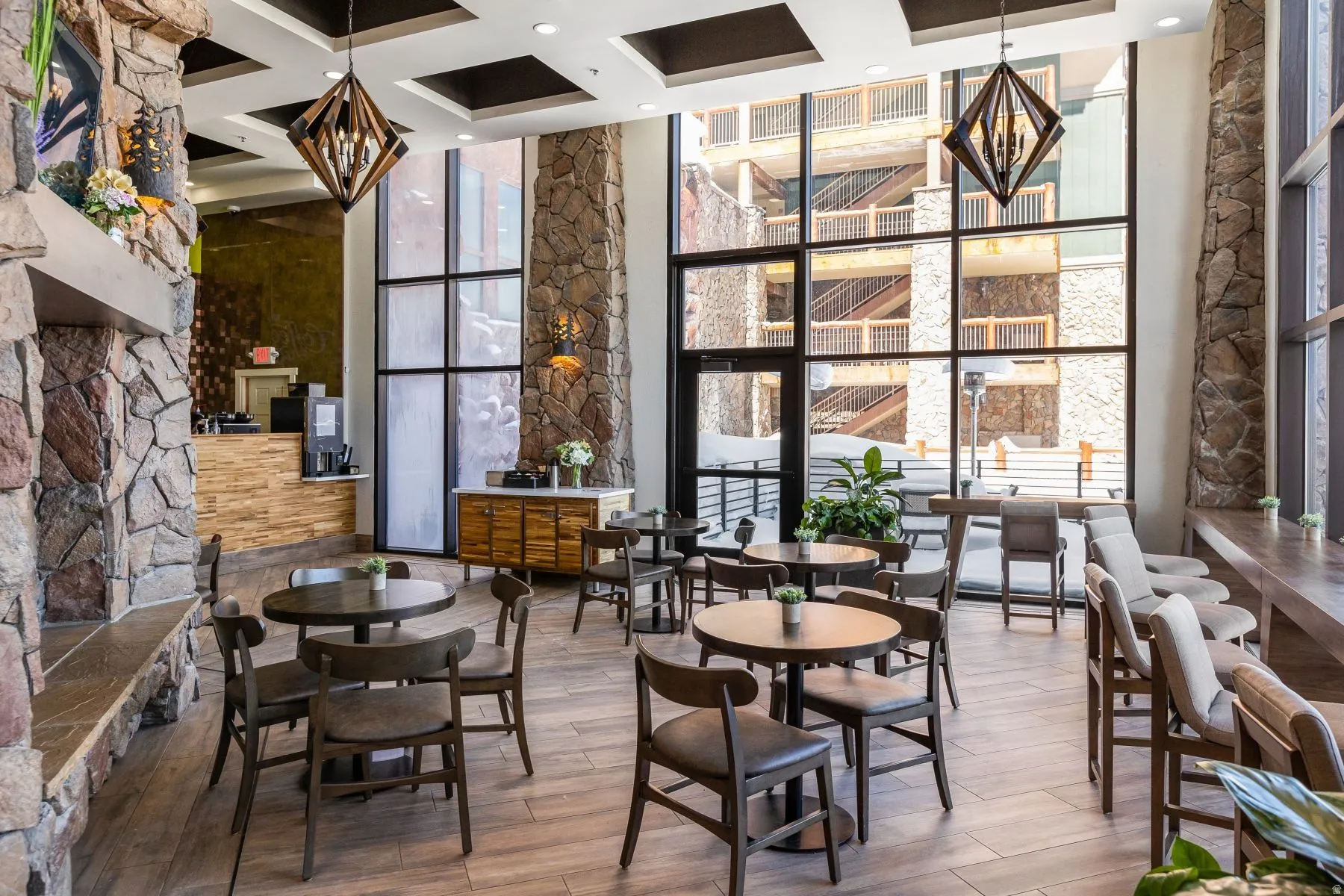 Spacious common area featuring floor-to-ceiling windows, stone-clad columns, coffered ceilings, and wood-finish flooring
