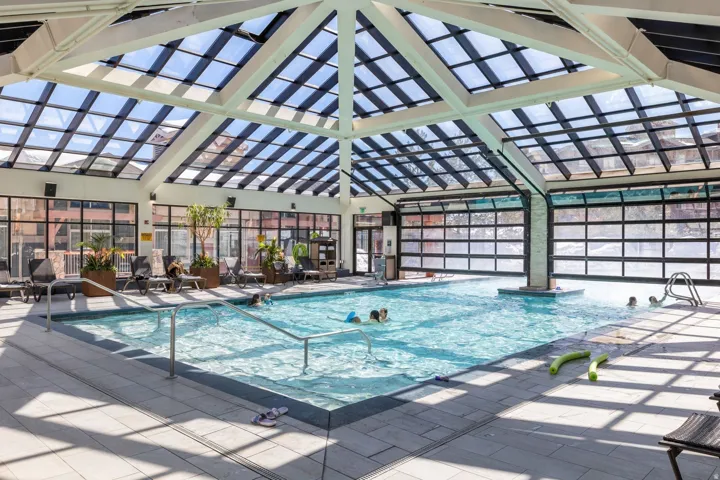 Indoor swimming pool featuring a glass-paneled ceiling, expansive window walls, and tiled flooring