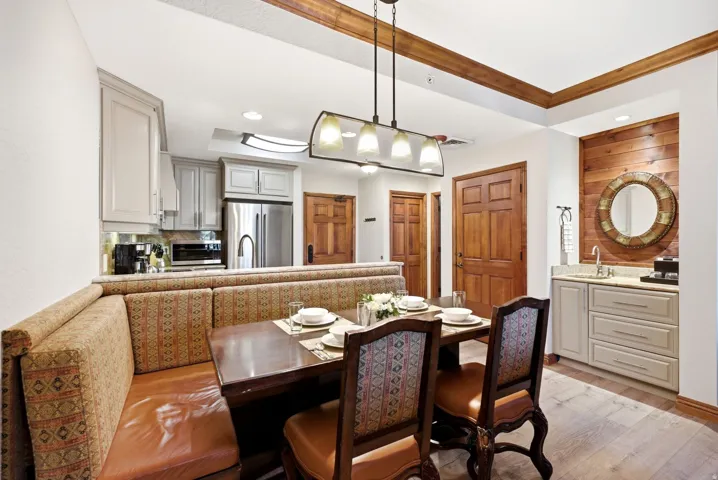 Open-concept dining area featuring a built-in banquette, wood-finish flooring, a contemporary chandelier, a wet bar with shaker-style cabinetry, and a kitchen with stainless steel appliances