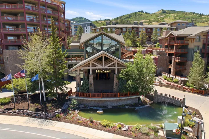 Mountain resort property featuring a grand entrance, stone accents, expansive balconies, a decorative pond with a fountain, and surrounding mature trees