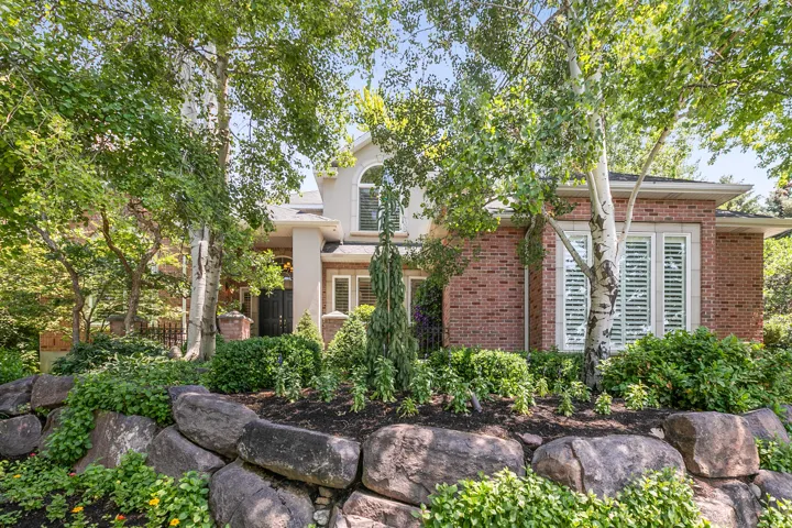 Brick and stucco exterior with multiple mature trees and an arched second-story window
