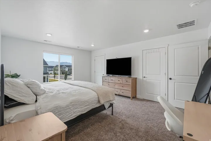 Bright bedroom with a large window, recessed lighting, and soft carpet flooring